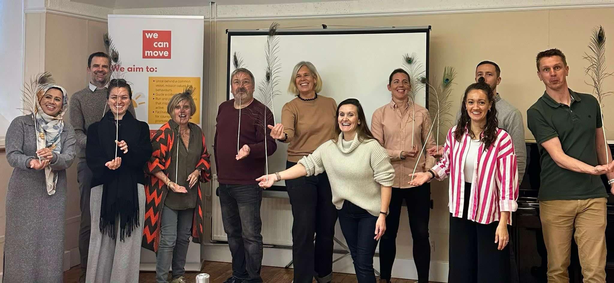 The Active Gloucestershire team smiling at the camera while balancing feathers on the palm of their hands.
