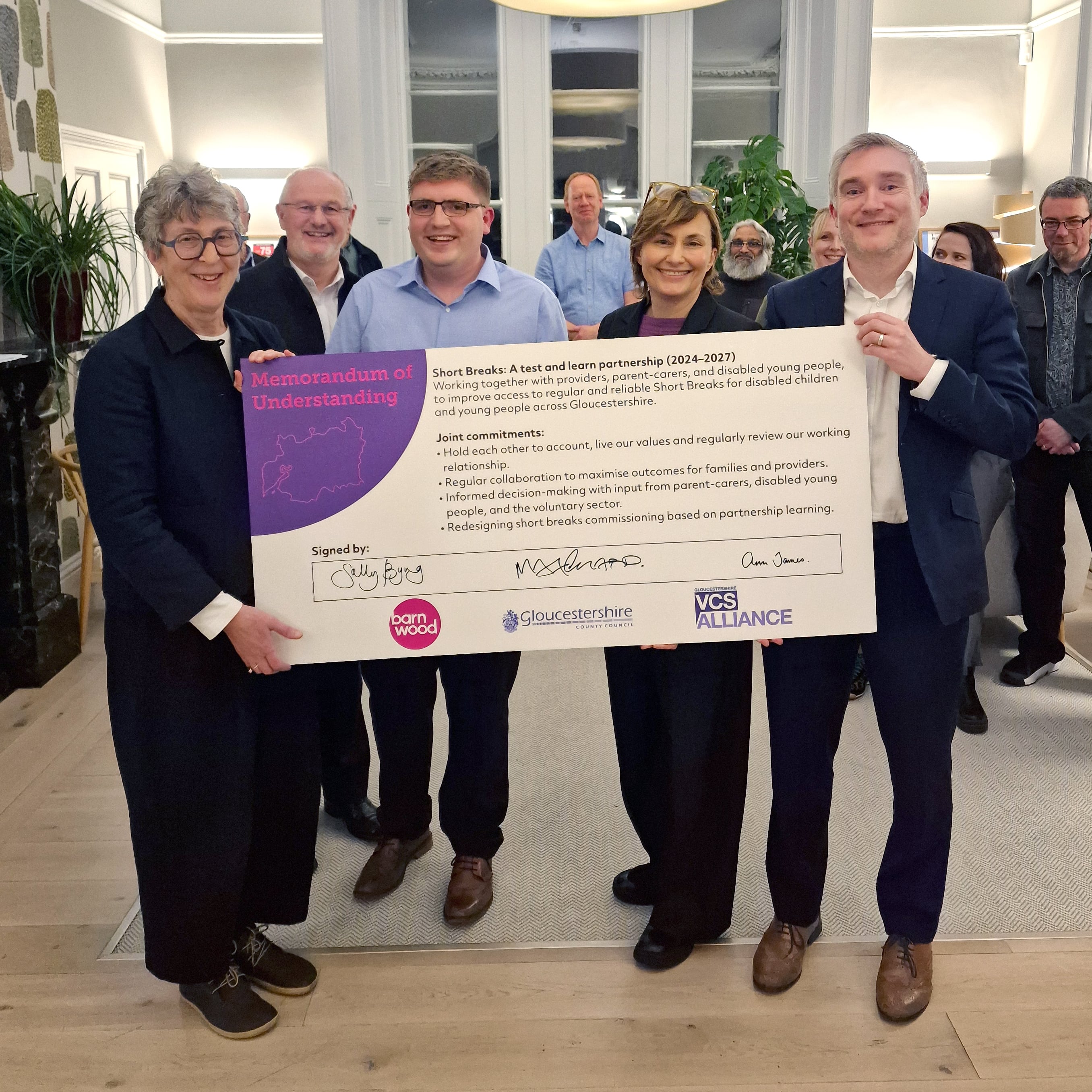 Partners from the Barnwood Trust and Gloucestershire County Council standing with Matt Lennard, holding the signed MoU document.